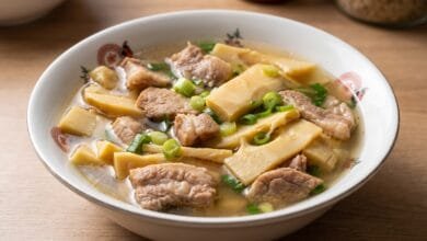 A bowl of Cambodian bamboo shoots soup with pork, showing tender pork slices and bamboo shoots in a clear broth topped with green onion.