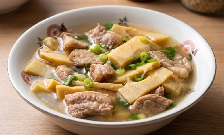 A bowl of Cambodian bamboo shoots soup with pork, showing tender pork slices and bamboo shoots in a clear broth topped with green onion.