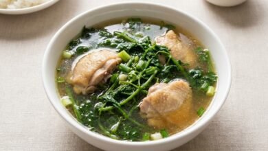 Overhead view of a bowl of Cambodian bitter vines soup with chicken, green onion, and clear broth.