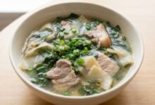 Overhead view of Cambodian bamboo shoot and slirk ngup soup in a ceramic bowl with pork, bamboo shoots, and green onion.