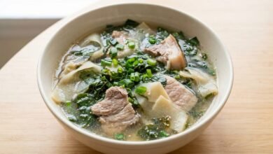 Overhead view of Cambodian bamboo shoot and slirk ngup soup in a ceramic bowl with pork, bamboo shoots, and green onion.
