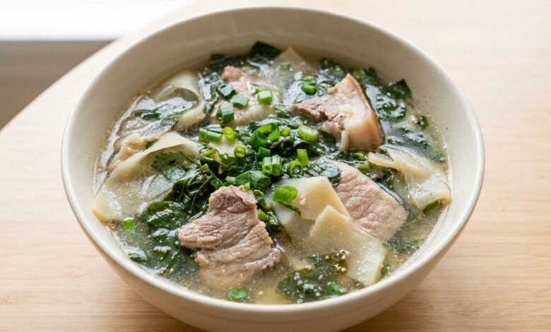 Overhead view of Cambodian bamboo shoot and slirk ngup soup in a ceramic bowl with pork, bamboo shoots, and green onion.