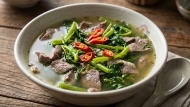 A bowl of Cambodian beef water spinach sweet sour soup with clear tamarind broth, sliced beef, and fresh herbs.
