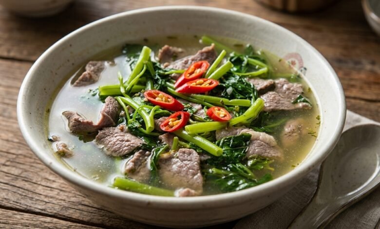A bowl of Cambodian beef water spinach sweet sour soup with clear tamarind broth, sliced beef, and fresh herbs.