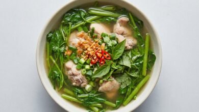 A bowl of Cambodian chicken sweet sour soup with water spinach, topped with fresh herbs and fried garlic.