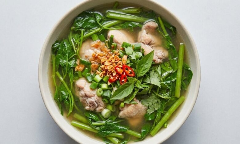 A bowl of Cambodian chicken sweet sour soup with water spinach, topped with fresh herbs and fried garlic.