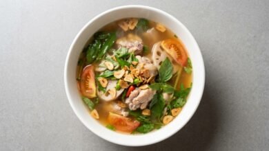 Overhead view of Cambodian hot sour chicken soup with lotus shoots, tomato, and fresh herbs in a bowl
