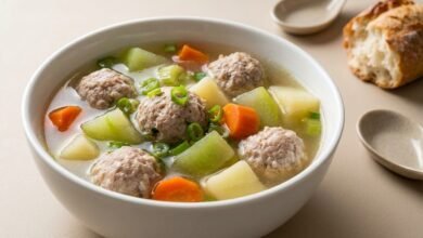 Overhead view of a bowl of Cambodian pork meatball soup with green papaya, carrot, potato, and celery in a clear broth.