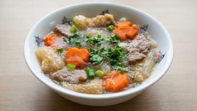 Overhead view of Cambodian bean thread noodles soup with pork, carrot, fried pork skin, and fresh herbs in a bowl.