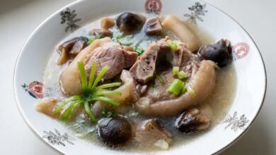 Overhead view of braised pork hock with straw mushrooms in a dark bowl, garnished with green onion.
