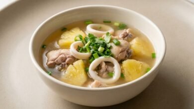 Overhead view of Cambodian pineapple soup with chicken, squid, and fresh herbs in a bowl.