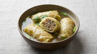 Overhead view of Cambodian pork stuffed cabbage soup with cabbage rolls tied with green onion in a light broth.