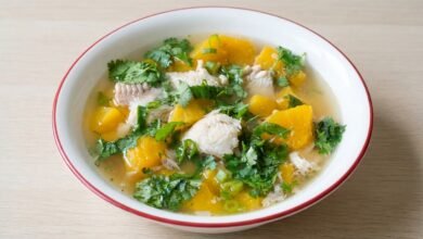 Overhead view of a bowl of Cambodian pumpkin soup with fish, showing orange pumpkin chunks, white fish, and cilantro garnish.
