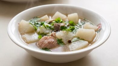 Overhead view of Cambodian daikon soup with pork hock, daikon cubes, green onion, and cilantro in a bowl.