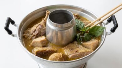 Overhead view of a Cambodian hot pot with duck pieces, taro cubes, and water spinach in a savory broth.