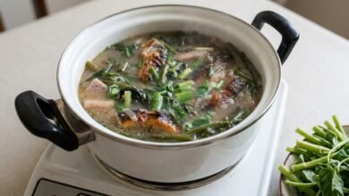 Overhead view of a Cambodian eel hot pot with taro root in a savory broth, topped with green onions and served with raw water spinach.