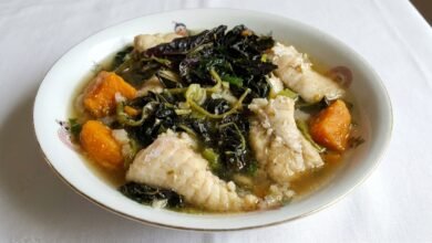 Overhead view of Cambodian fish and Asian purple spinach soup with catfish, sweet potato, and green onion in a bowl.
