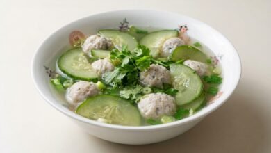 A bowl of Cambodian fish ball and cucumber soup with clear broth, fish balls, cucumber slices, and fresh herbs.