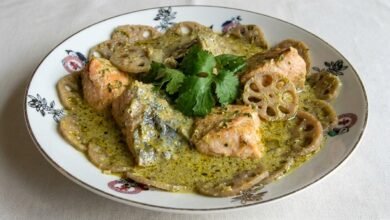 A bowl of green curry salmon with lotus shoot in a creamy coconut sauce.