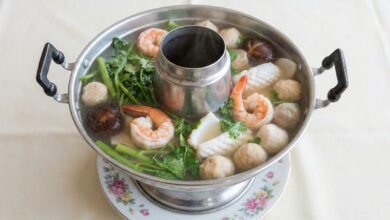 Overhead view of a Khmer seafood hot pot with clear broth, shrimp, squid, fish balls, and vegetables.