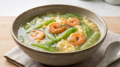A bowl of Cambodian loofah soup with shrimp, showing tender loofah strips, pink shrimp, and egg ribbons in a clear broth.