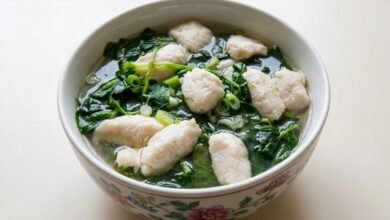 Overhead view of Cambodian pea shoots and basa fish soup in a bowl with green onion.