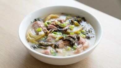 Overhead view of Cambodian pork hock soup with pickled mustard greens and green onion in a bowl.