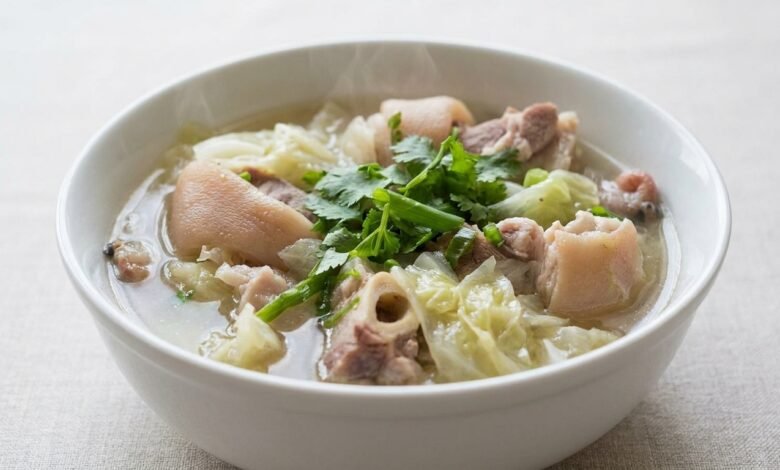 Overhead view of Cambodian pork hocks and cabbage soup in a bowl, garnished with cilantro and green onion.