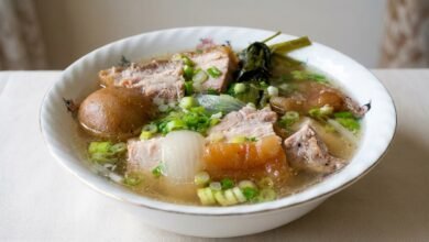 Overhead view of Cambodian preserved lime soup with roasted pork, onion, and green onion in a bowl.