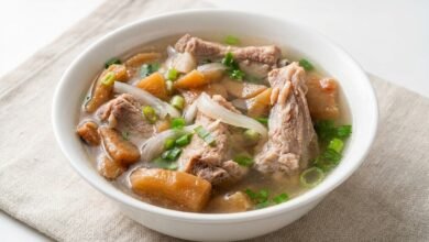 A bowl of Cambodian preserved turnip with pork ribs soup, showing tender pork ribs, preserved turnip pieces, and green onion in a golden broth.