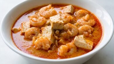 Bowl of Cambodian red curry with pink shrimp, white tofu cubes, and orange coconut broth.