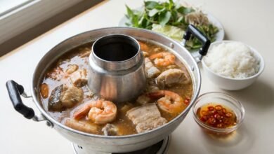 Overhead view of a Cambodian seafood hot pot with catfish, shrimp, pork belly, and light fermented fish broth.