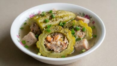 Overhead view of shrimp stuffed bitter melon soup with taro in a clear broth, topped with green onion.