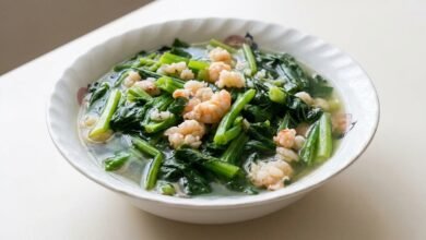A bowl of Cambodian shrimp with yu choy soup showing pink shrimp, green leafy vegetables, and a clear broth.