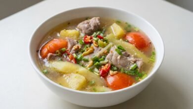 Overhead view of Cambodian sweet sour pineapple pork ribs soup with clear broth, pork ribs, pineapple, herbs, and chili in a bowl.