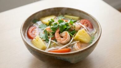 A bowl of Cambodian sweet sour and spicy shrimp soup with shrimp, pineapple, tomato, bean sprouts, and fresh herbs.