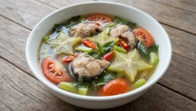 A bowl of Cambodian sweet sour spicy star fruit soup with catfish, star fruit slices, and fresh herbs.