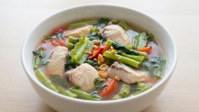 Overhead view of a bowl of Cambodian sweet sour fish soup with water spinach and fresh herbs.