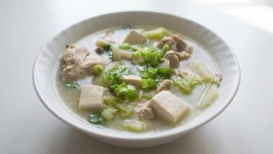 Overhead view of a bowl of Khmer tofu chicken soup with clear broth, chicken chunks, tofu, and Napa cabbage.