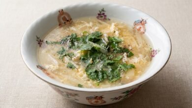 Overhead view of white asparagus and crab meat soup in a bowl, garnished with green onion and cilantro.