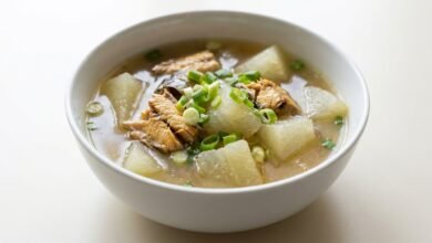 A bowl of Cambodian winter melon and steamed mackerel soup with tender gourd chunks, golden fish, and green onion in a light broth.
