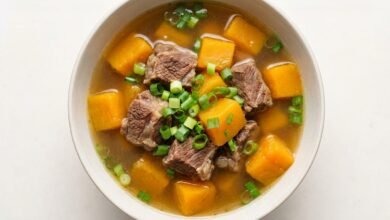 A bowl of Pumpkin Beef Shank Soup viewed from above, showing tender beef, pumpkin cubes, and green onion in a golden broth.