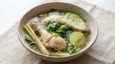 Overhead view of Cambodian chicken lemon soup with clear broth, chicken, lemongrass, cucumber, and fresh herbs.