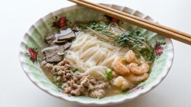 Overhead view of a bowl of Cambodian Phnom Penh noodle soup with pork, shrimp, and herbs.