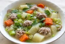 Overhead view of Cambodian pork and vegetable soup with chayote, carrot, and sweet basil in a bowl, served with rice.