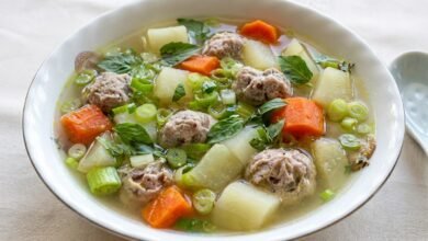 Overhead view of Cambodian pork and vegetable soup with chayote, carrot, and sweet basil in a bowl, served with rice.