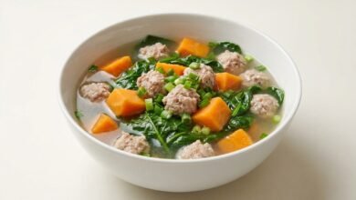Overhead view of a bowl of Cambodian Malabar spinach soup with pork, sweet potato, and green onion.