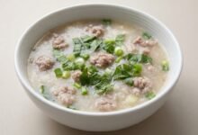 Overhead view of Cambodian white yam and pork soup in a ceramic bowl, topped with chopped green onion and saw-leaf herb.
