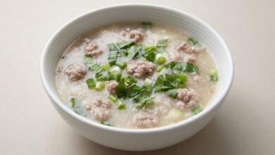 Overhead view of Cambodian white yam and pork soup in a ceramic bowl, topped with chopped green onion and saw-leaf herb.