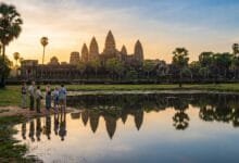 Sunrise view of Angkor Wat temple in Cambodia with a small group of visitors reflecting in the foreground pond